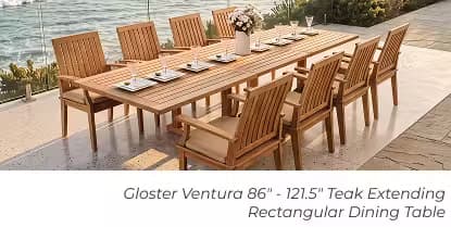 Large rectangular teak dining table with eight chairs, place settings and a floral centerpiece overlooking the water.