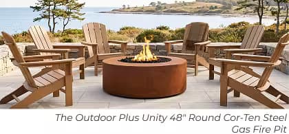 Corten steel Outdoor Plus Unity round gas fire pit surrounded by Adirondack chairs overlooking the coast.