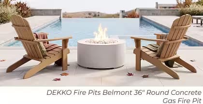 White DEKKO Belmont round gas fire pit between two Adirondack chairs beside an infinity pool.