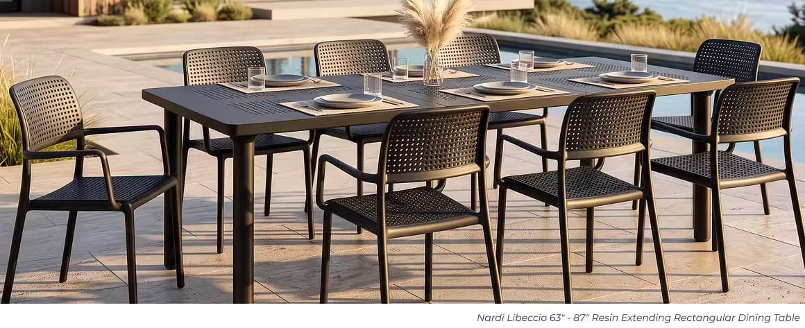Dark resin extending outdoor dining table with eight perforated chairs beside a pool.